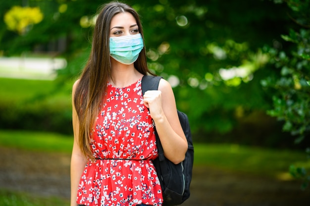 Photo female student walking outdoor in the park and wearing a mask to protect herself from coronavirus