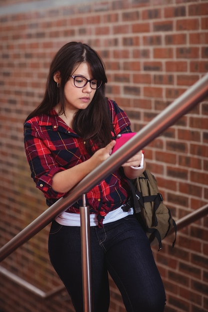 Female student walking on staircase while using mobile phone