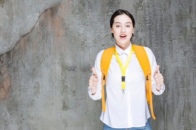 Female student wearing yellow backpack giving thumbs up. High quality photo