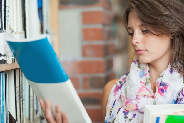 図書館の棚で本を持っている女性学生