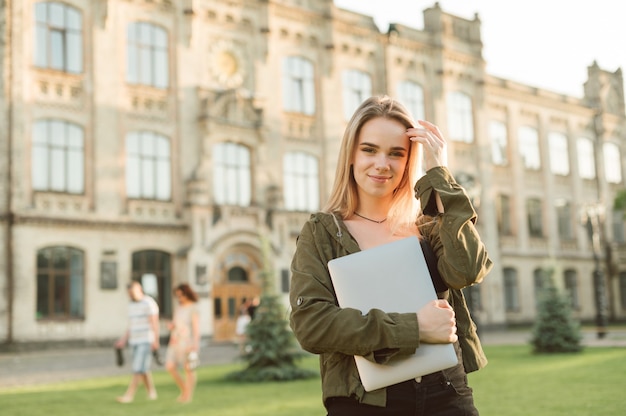 Female student with broad smile standing in front of university