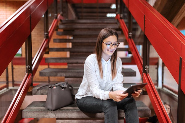 Foto studentessa con occhiali e capelli castani facendo uso della compressa mentre sedendosi sulle scale