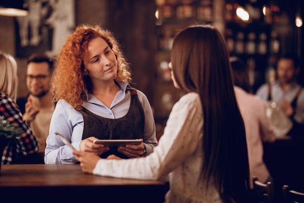 Female student working as a waitress and communicating with female customer in a bar