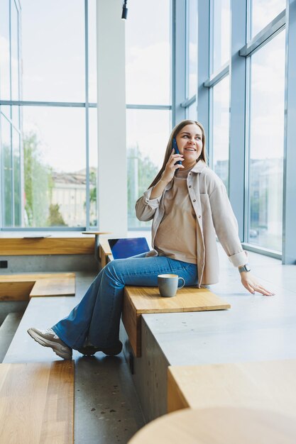 A female student works in a bright cafe with large windows online Remote work with a laptop in a cozy work cafe