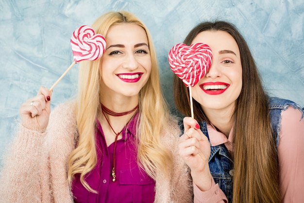 Photo female stylish friends having fun with candy on the blue wall background