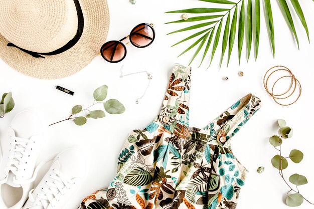 Female summer street style Sundressdress straw hat sneakers sunglasses and tropical leaf Top view flat lay