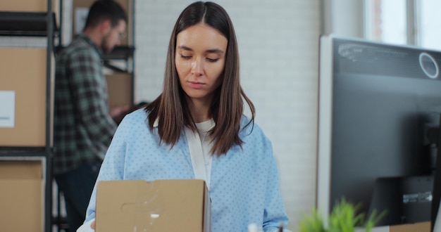 Female support service manager checks the order number on the parcel using a computer prepares a box for mailing Warehouse work