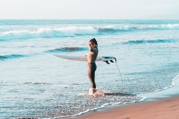 female surfer on the beach standing with surfboard watching the horizon at sunset