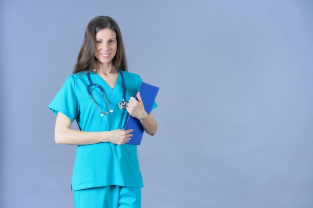 Female surgeon in aquamarine scrubs holding clipboard smiling at camera with stethoscope