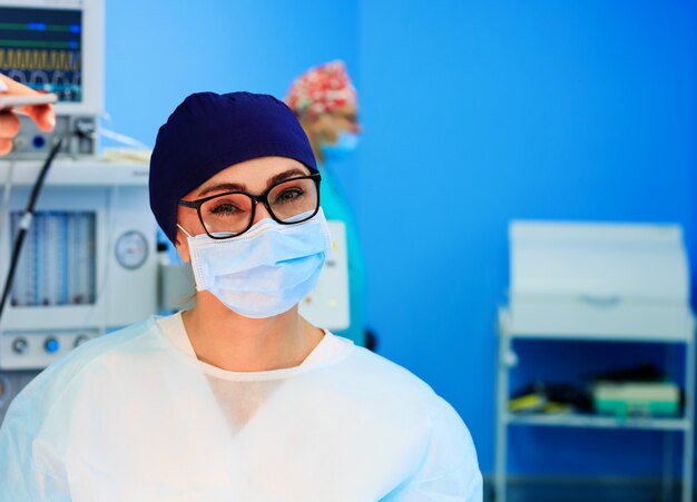 Female surgeon smiling in a mask on the background of medical equipment