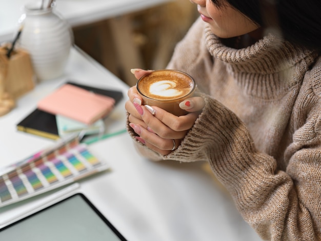 Женщина в свитере держит чашку горячего кофе латте
