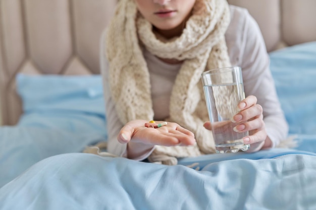 自宅のベッドでコップ1杯の水と一緒に錠剤カプセルを服用している女性