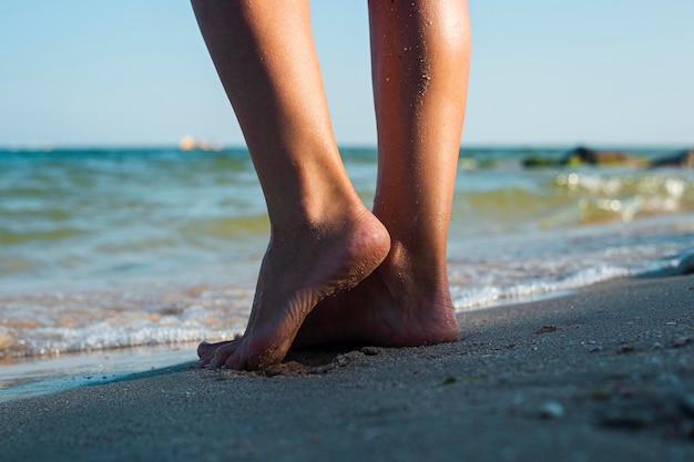 Female tanned legs stand near the sea on a sandy beach