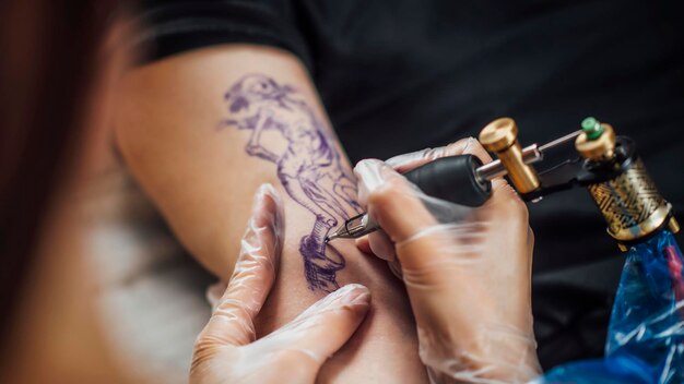 Foto artista del tatuaggio femminile tatuando il braccio dell'uomo in studio