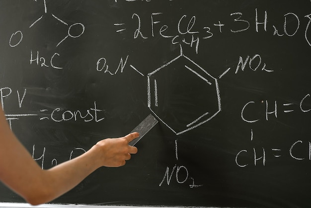 Female teacher explane chemical formulas near chalkboard