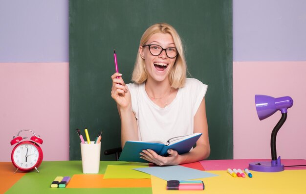 彼女の机の女教師が生徒の仕事をマークしている学校の学生のカメラに微笑んでいるかわいい先生図書館の本からメモを取っている女子学生