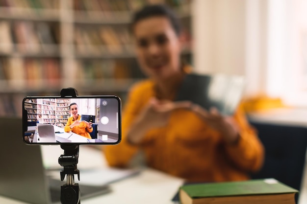 Foto insegnante femminile che riprende una lezione online per gli studenti che utilizzano il cellulare sul treppiede e mostrano il fuoco selettivo del tablet