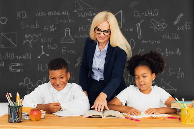 Un'insegnante donna insegna ai bambini delle scuole che siedono a una scrivania e risolvono problemi squadra internazionale ritorno a scuola