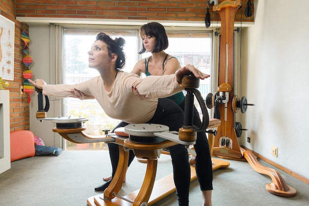 female teacher teaching her female student correct technique of exercising on machine