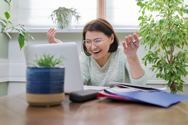 Female teacher teaching online sitting at home at table with\
laptop