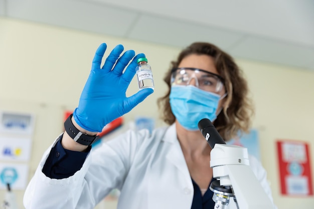 Female teacher wearing face mask and protective glasses holding a vial bottle in laboratory