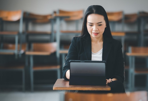 A female teacher with a tablet sits in an empty classroom at the university. while waiting to teach the students at the class