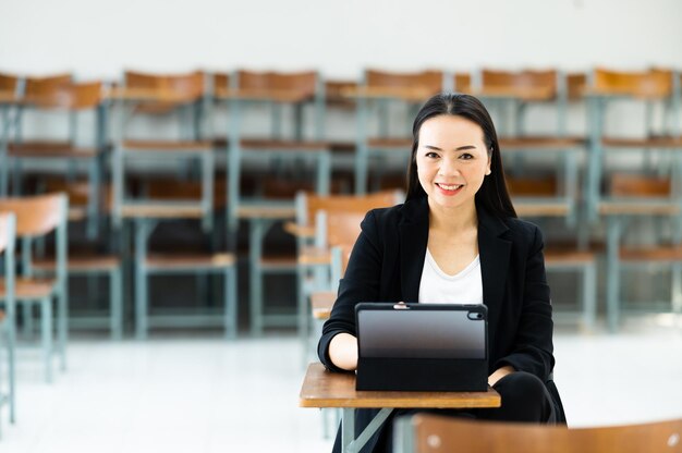 タブレットを持った女教師が大学の空いている教室に座っている。クラスで生徒に教えるのを待っている間