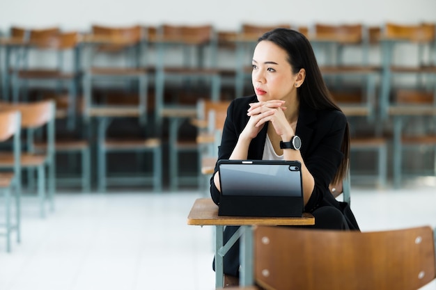 Учительница с планшетом сидит в пустом классе университета. в ожидании обучения студентов в классе