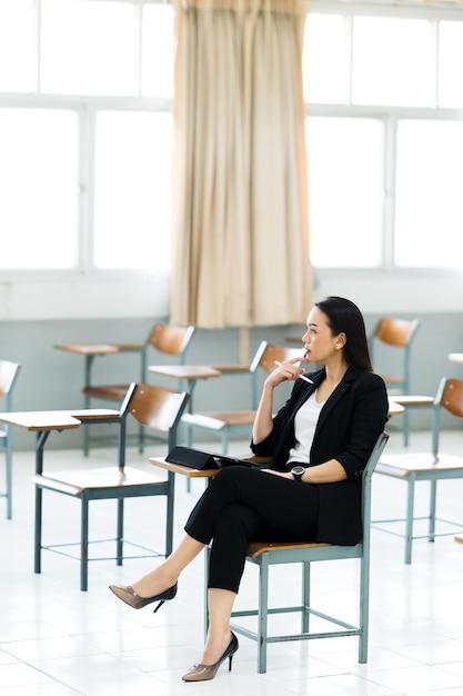 A female teacher with a tablet sits in an empty classroom at the university. while waiting to teach the students at the class