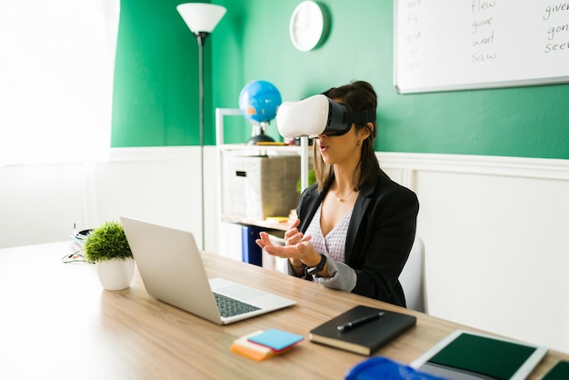 Female teacher with VR glasses using technology to teach an online lesson. Young woman on a virtual reality classroom