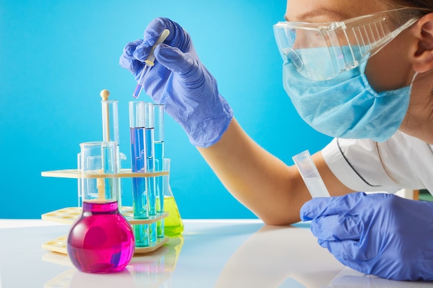 Female tech or scientist loads liquid sample into bottle with  pipette. Test-tubes on blue background.