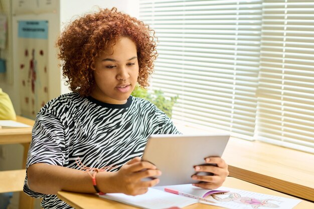 Female teenager in casualwear looking through information on screen of tablet