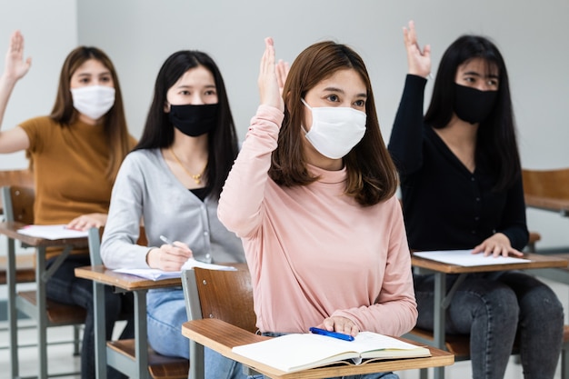 Студентки колледжа носят маску и соблюдают дистанцию во время обучения в классе и кампусе колледжа, чтобы предотвратить пандемию COVID-19