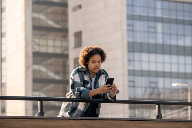 Female teenager scrolling in smartphone while bending over railings