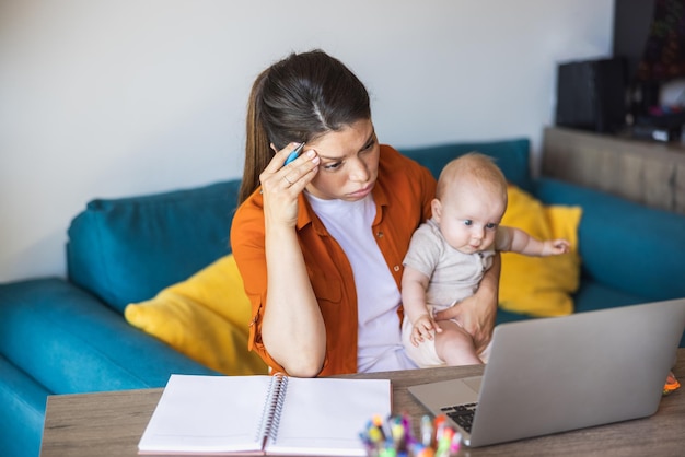 Photo female tired entrepreneur working on laptop and taking care of her baby at home.