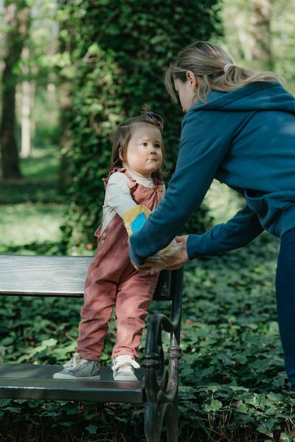 ベルベットのオーバーオールを着た女の幼児が母親と一緒にベンチに座っている