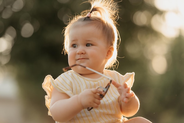 A female toddler in yellow clothes is playing with sunglasses in the park