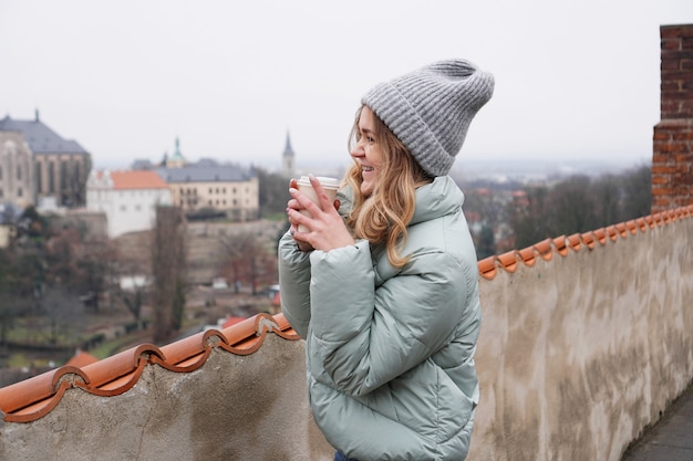 Female tourist against the background of town in the Czech Republic - Kutna Hora. She drinks mulled wine - autumn season