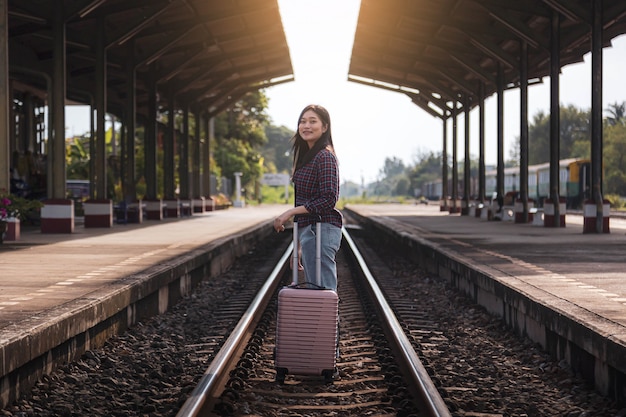 ピンクの鞄を持った女性観光客が駅で電車を待っています。