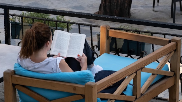 Foto libro di lettura turistica femminile sul divano di legno in vacanza