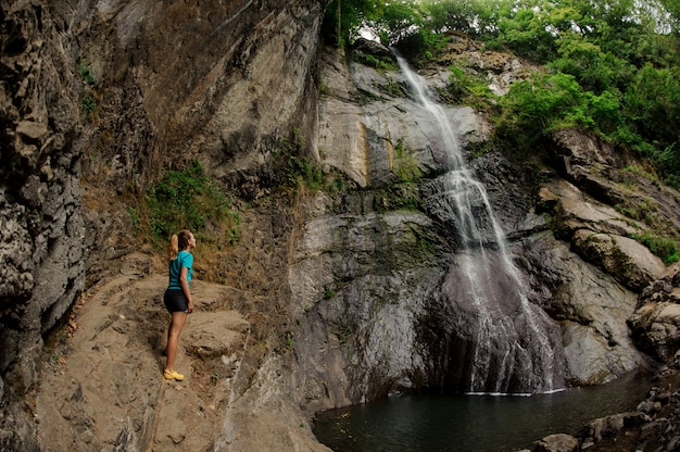 Female tourist in sportswear stands near waterfall