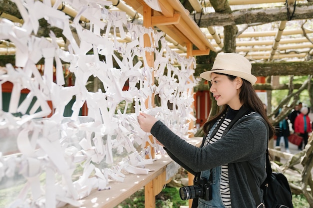 female tourist standing in front of musubidokoro, place where people tie their unwanted omikuji up to leave bad luck behind. woman holding and reading a fortune slip with bad result