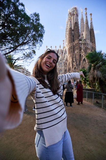 female tourist taking a happy selfie with sagrada familia in barcelona spain