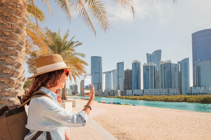 Photo female tourist taking pictures of abu dhabi skyline with smartphone under palm trees