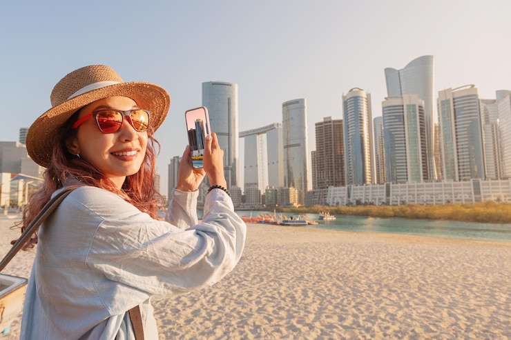 Photo female tourist taking pictures of abu dhabi skyline with smartphone under palm trees