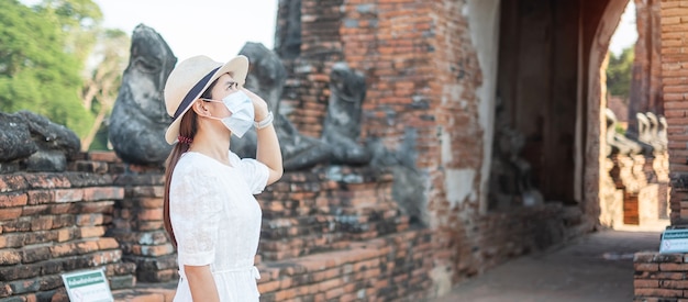 Turista femminile che indossa la mascherina chirurgica che visita il tempio di wat chaiwatthanaram