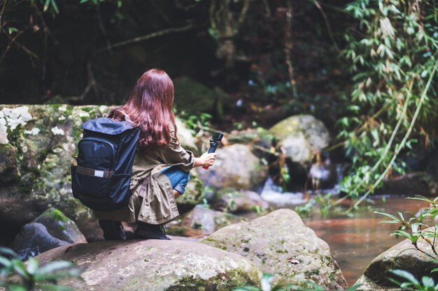 アクションカメラで森の滝のバックパック撮影ビデオを持つ女性観光客