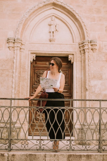 이탈리아 오스투니(Ostuni)의 산 프란체스코 다시시(San Francesco d'Assisi) 교회 옆 도시 지도를 들고 있는 여성 관광객