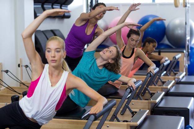 Female trainer assisting group of women with stretching exercise on reformer