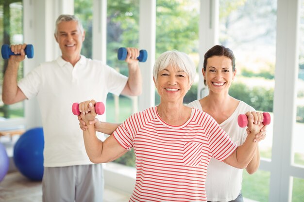 Female trainer assisting senior couple in performing exercise